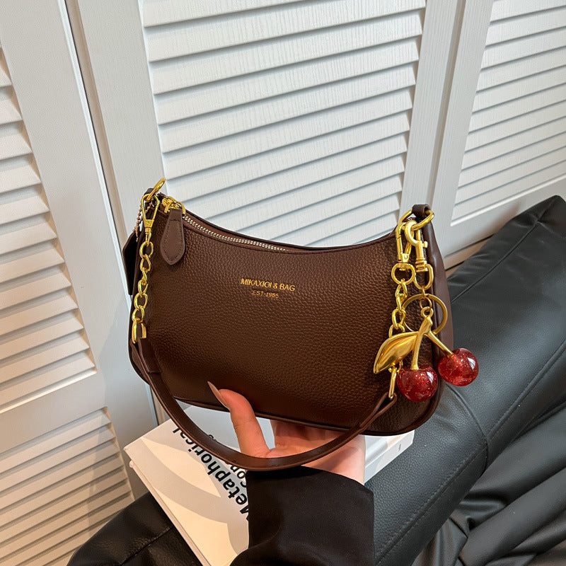 Brown PU dumpling bag with cherry pendant, gold chain strap, small crossbody with zipper, polyester lining.