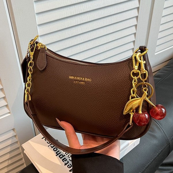 Brown dumpling crossbody bag with gold chain strap and cherry pendant charms.